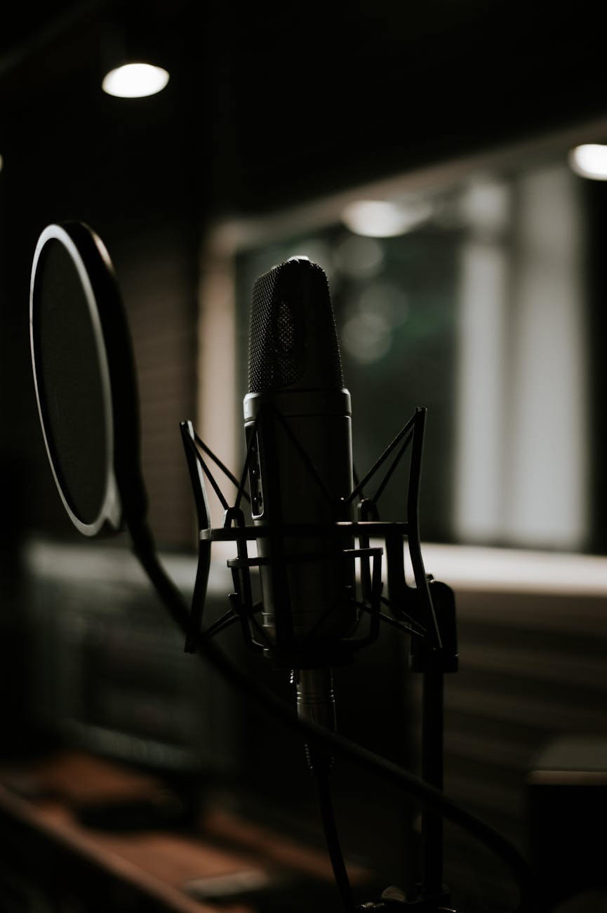 A professional studio condenser microphone with a black pop filter in a recording booth, representing the production phase of self-publishing an audiobook.